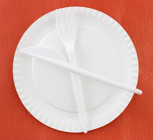 disposable plastic cutlery on white paper plate on red background