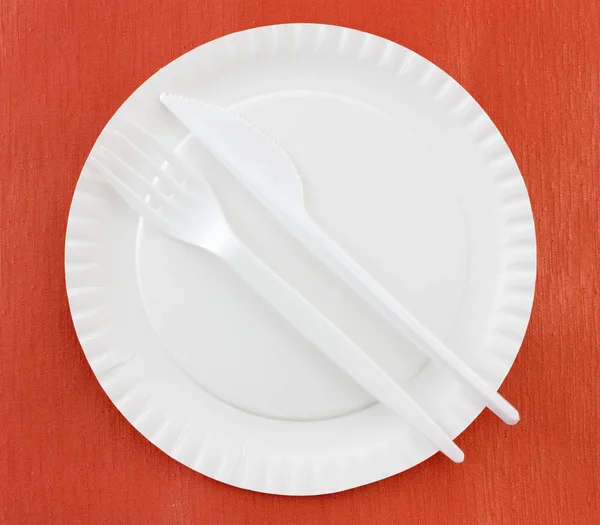 disposable plastic cutlery on white paper plate on red background