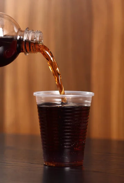 Pouring cola from bottle into plastic cup.