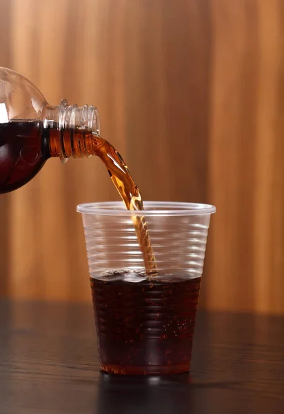 Pouring cola from bottle into plastic cup.