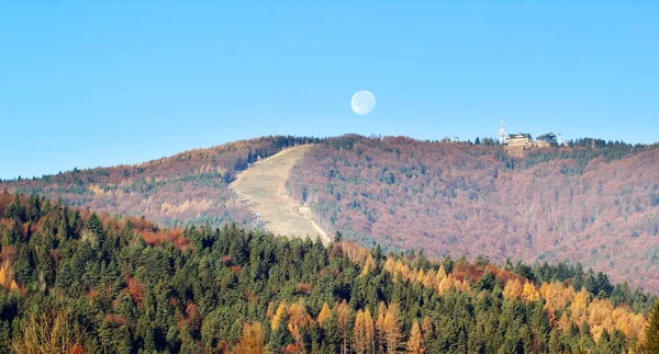 autumn mountainous landscape with trees and moon in blue sky
