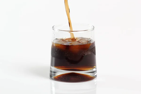 Pouring cola into glass with ice cubes. Isolated on white background.