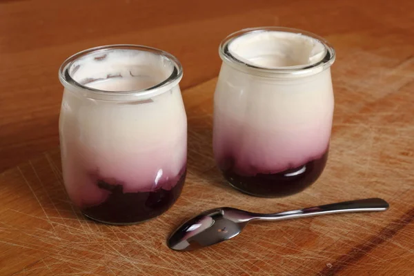 在木制切菜板上用勺子打开小玻璃瓶的果酱酸奶 — 图库照片