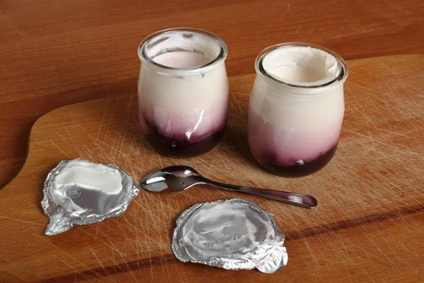 在木制切菜板上用勺子打开小玻璃瓶的果酱酸奶 — 图库照片