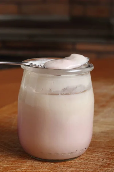 木制切菜板上打开的小玻璃瓶上装有酸奶的勺子 — 图库照片