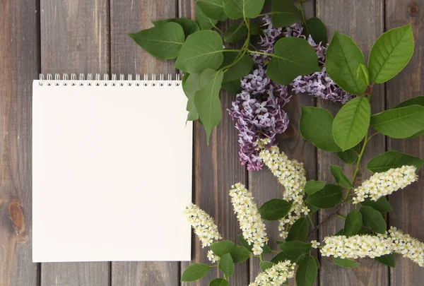 white notebook and branches of lilac and bird cherry trees on the background of gray wooden boards
