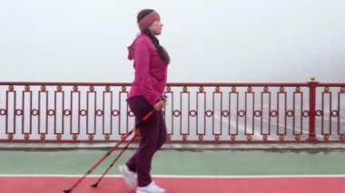 Batonlu yürüyüş. Nordic Polonyalılar ile genç tombul beyaz kadın yürüyüş. Yan takip shot. Yavaş hareket