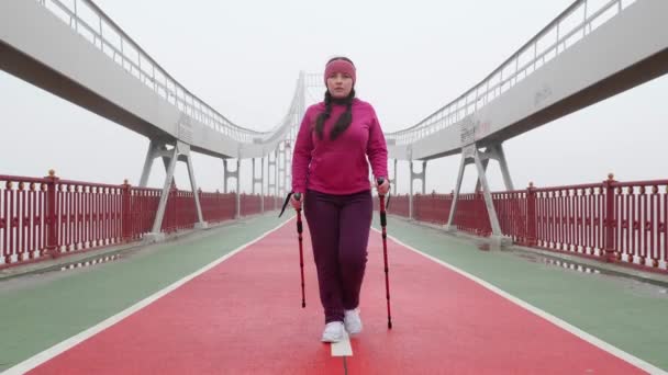 Nordic Walking. Jonge mollige Kaukasische vrouw wandelen met de Nordic Polen. Voorzijde Volg schot. Slow Motion — Stockvideo
