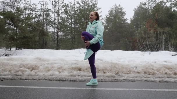 Senior velha mulher caucasiana aquece alongamento antes de correr no parque de inverno nevado. Um tiro lateral. Movimento lento — Vídeo de Stock