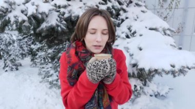 Sokakta kışın sıcak çay veya kahve içecek çekici güzel kız, o kırmızı ceket Noel ağacı yakın standları Örme Eldivenler giyer