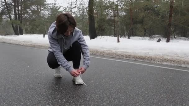 Unga attraktiva kaukasiska flicka skosnören skor innan du kör i den snöiga parken på vintern. — Stockvideo