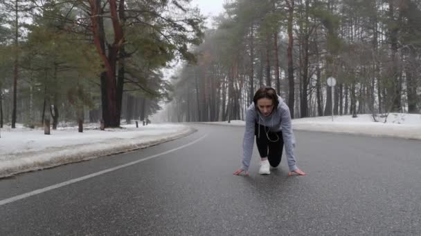 Unga attraktiva kaukasiska flicka börjar springa i den snöiga parken på vintern med hörlurar. Följ shot. — Stockvideo