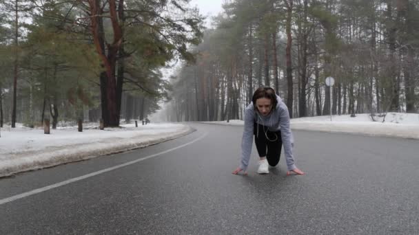 Unga attraktiva kaukasiska flicka börjar springa i den snöiga parken på vintern med hörlurar. Följ bilden. Slow Motion (långsam) — Stockvideo