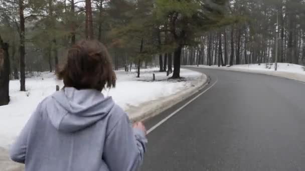 Unga attraktiva kaukasiska flicka som kör i den snöiga parken på vintern med hörlurar. Stäng upp tillbaka Följ shot. — Stockvideo