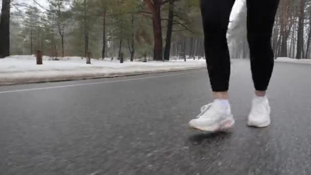 Joven atractiva chica caucásica corriendo en el parque nevado en invierno con auriculares. Primer plano piernas Frente seguir tiro . — Vídeo de stock