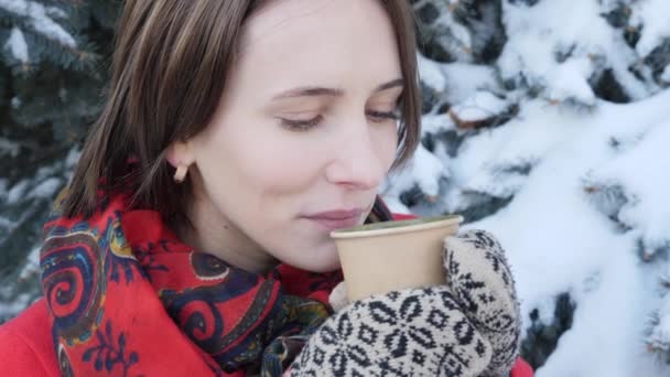 Nahaufnahme des Gesichts eines Mädchens, das im Winter auf der Straße heißen Tee oder Kaffee trinkt, sie trägt Strickhandschuhe. — Stockvideo