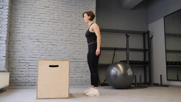 Fit athletische Kaukasierin macht Boxsprünge in der Turnhalle. Intensive Bewegung gehört zu ihrem täglichen Crosstraining. Seitenansicht — Stockvideo