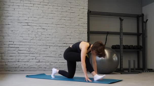 Stuoia di yoga giovane donna atletica allungamento dell'anca, muscoli del tendine del ginocchio, muscoli delle gambe all'interno di una palestra. Esercizi di stretching — Video Stock