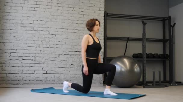 Wanita kulit putih yang melakukan latihan otot kaki latihan latihan di gym. Gadis aktif melakukan depan satu kaki menerjang langkah pandangan samping — Stok Video