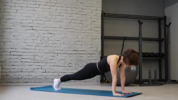 Zijaanzicht van jonge atletische Kaukasische vrouw in sportkleding Keeping plank positie tijdens het sporten binnenshuis in Gym — Stockvideo