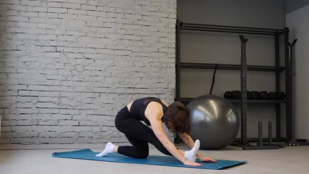 Yoga mat wanita atletik muda peregangan pinggul, otot hamstring, otot kaki di dalam ruangan di gym. Latihan peregangan — Stok Video