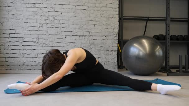 Stuoia di yoga giovane donna atletica allungamento dell'anca, muscoli del tendine del ginocchio, muscoli delle gambe all'interno di una palestra. Esercizi di stretching — Video Stock