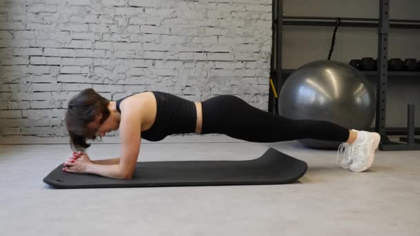 年轻运动白种人妇女穿着运动服, 在健身房室内锻炼时保持木板位置的侧视图 — 图库视频影像