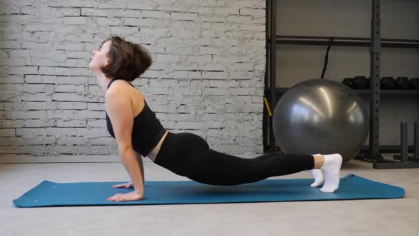 Stuoia di yoga giovane donna atletica allungamento dell'anca, muscoli del tendine del ginocchio, muscoli delle gambe all'interno di una palestra. Esercizi di stretching — Video Stock