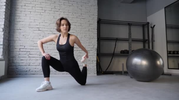 Γιόγκα χαλάκι νεαρή αθλητική γυναίκα που εκτείνεται ισχίου, κοιλιακοί μύες, μύες πόδι σε εσωτερικούς χώρους σε ένα γυμναστήριο. Ασκήσεις τεντώματος — Αρχείο Βίντεο