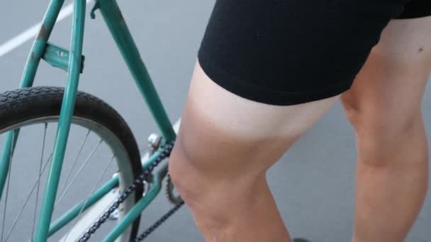 Κλείστε θέα από ένα πράσινο κομμάτι σταθερό ρετρό ποδήλατο σε ένα Ποδηλατοδρόμιο και ένα πόδι ποδηλάτης με ήλιο — Αρχείο Βίντεο