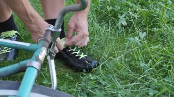 Cordón ciclista ata sus zapatos de ciclismo negro en hierba verde cerca de la bicicleta vintage — Vídeo de stock