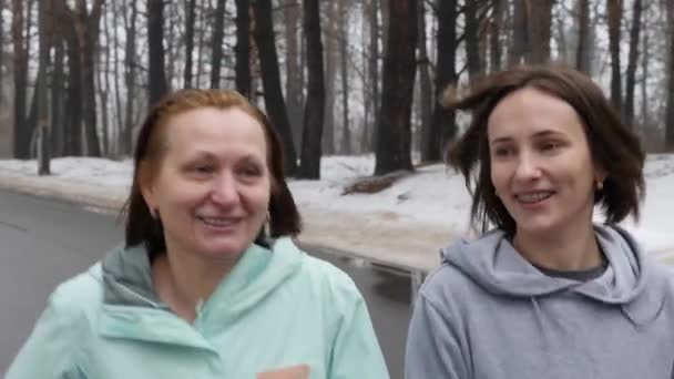 Heureuses femmes âgées et jeunes femmes caucasiennes courant dans le parc enneigé en hiver parlant et souriant. Gros plan Avant suivre la prise de vue. Mouvement lent — Video