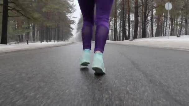 Stará Kavkazská dívka, která v zimě běží v zasněženém parku se sluchátky. Nohy zavřít zadní záběr. — Stock video