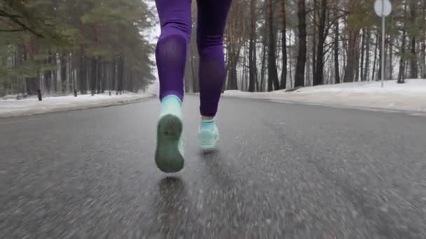 Senior vieja chica caucásica corriendo en el parque nevado en invierno con auriculares. Pats Close up Back sigue el disparo. Moción lenta — Vídeos de Stock