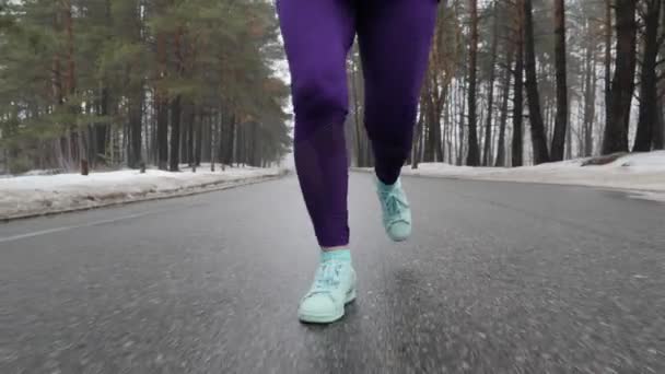 Старшая белая девушка бегает в снежном парке зимой в наушниках. Ноги спереди спереди следуют за выстрелом. Slow Motion — стоковое видео