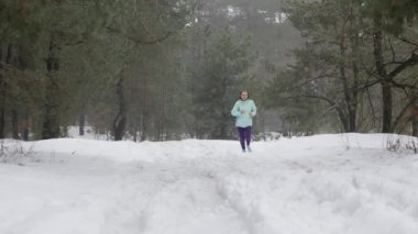 İz koşunun. Yaşlı eski beyaz kadın ormanda karda koşuyor. Ön takip çekimi.