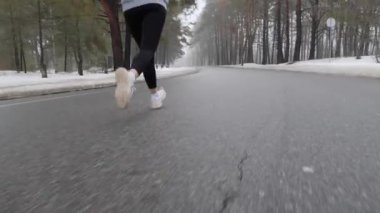 Genç çekici Kafkas kız kulaklıklar ile kışın karlı parkta çalışan. Yakın çekim geri takip çekim.