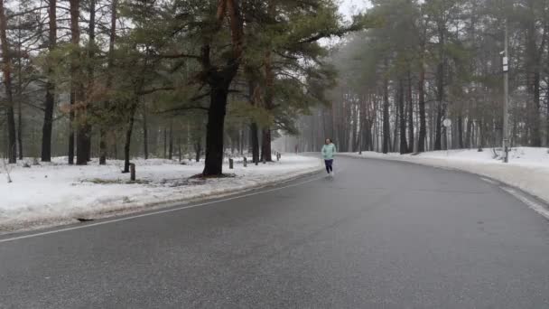 Senior vieja mujer caucásica corriendo en el parque nevado en invierno con auriculares. Frente seguir disparo . — Vídeos de Stock