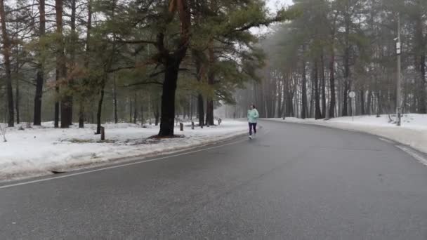 Senior vieja mujer caucásica corriendo en el parque nevado en invierno con auriculares. Disparo de seguimiento frontal. Movimiento lento — Vídeos de Stock