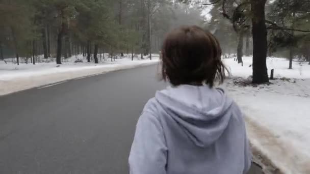 Giovane ragazza caucasica attraente in esecuzione nel parco innevato in inverno con le cuffie. Close up Indietro segui colpo . — Video Stock