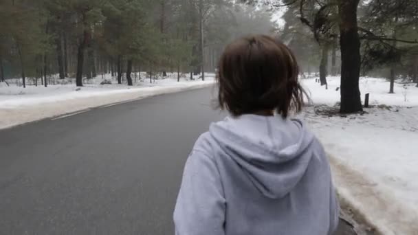 Unga attraktiva kaukasiska flicka som kör i den snöiga parken på vintern med hörlurar. Close up back Följ Shot. Slow Motion (långsam) — Stockvideo