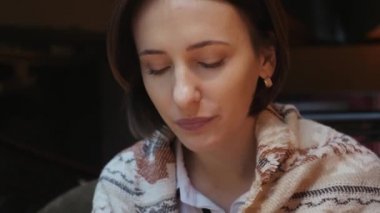 Genç çekici kadın bir restoranda kahve çayı içiyor. Omuzları sıcak bir örme eşarp ile kaplıdır