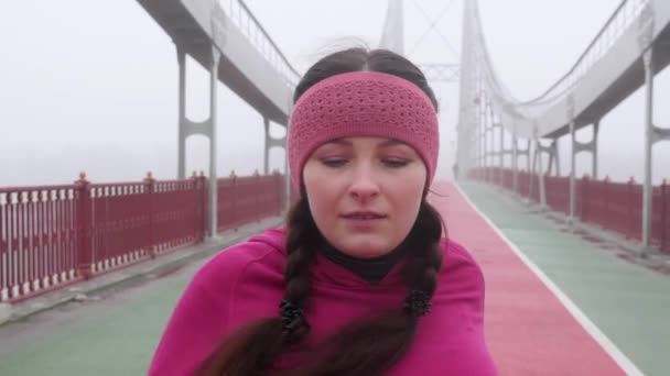 Junge mollige Kaukasierin, die auf einer Brücke läuft. Schuss nach vorne. Zeitlupe. lila Outfit — Stockvideo