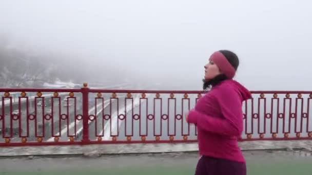 Joven gordita caucásica chica corriendo en un puente. Un tiro lateral. Traje púrpura — Vídeos de Stock