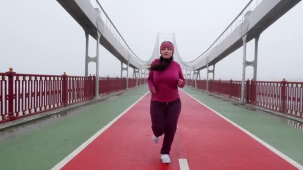 年轻的胖胖的白种人女孩在桥上奔跑。前拍慢动作。紫色的衣服 — 图库视频影像