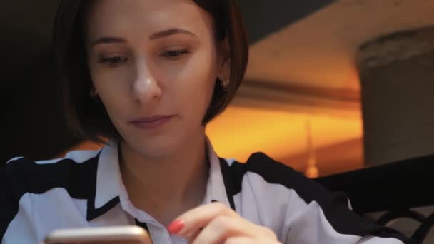 Joven atractiva mujer utiliza su teléfono móvil en un acogedor restaurante cafetería. Ella está sorprendida y enojada . — Vídeos de Stock