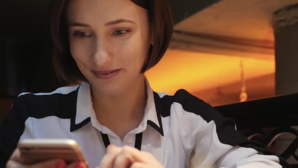 Genç çekici kadın rahat bir kafe restoranda cep telefonu kullanır. O gülümsüyor ve mutlu — Stok video