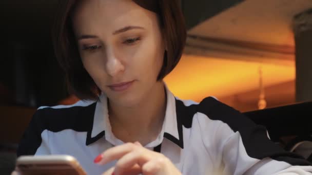 Genç çekici kadın rahat bir kafe restoranda cep telefonu kullanır. O gülümsüyor ve mutlu — Stok video