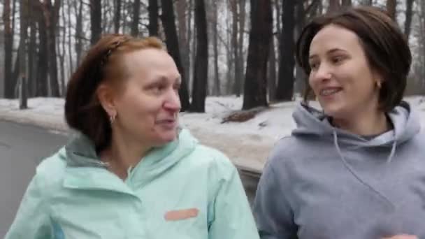Heureuses femmes âgées et jeunes femmes caucasiennes courant dans le parc enneigé en hiver parlant et souriant. Gros plan Front follow shot . — Video