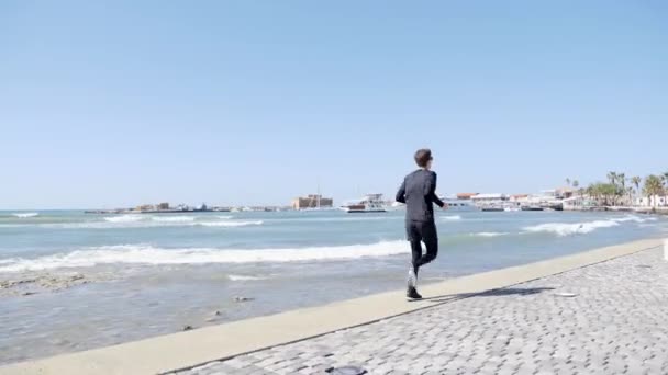 Joven atractivo en forma caucásico hombre de negro corriendo en un muelle. Vuelta atrás — Vídeos de Stock